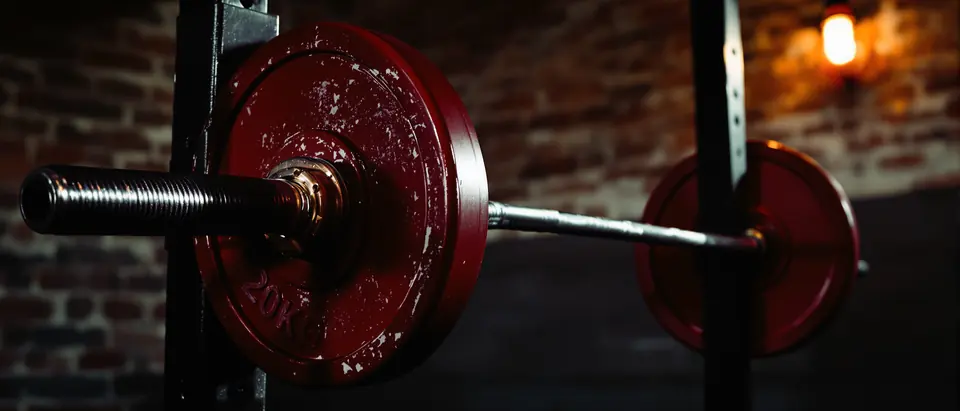 A loaded barbell in a power rack, warm side light, chalked steel.